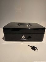 Front view of closed black Garrison lock box with one key placed in front