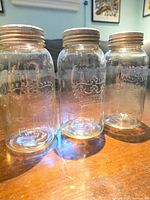Three clear glass mason jars standing side by side showing embossed logos and zinc lids