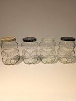 Front view of four clear bear-shaped jars showing lids and glass detail