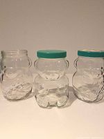 Front view of three bear-shaped glass jars showing lids and overall condition