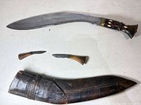 Kukri knife, two small knives, leather sheath laid out