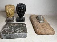 Group view of all four pieces: etched slab, two stone heads on bases, stone head on wood board