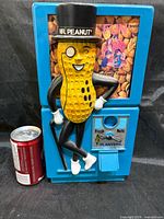 Front view of blue plastic Mr. Peanut vending machine with soda can for scale