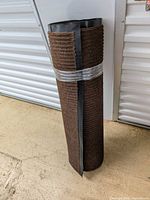 Full rolled rug standing upright showing brown ribbed surface