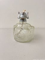 Front view of clear pressed glass oil lamp showing embossed panels and metal burner