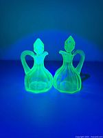 Pair of green uranium glass cruets glowing under UV light
