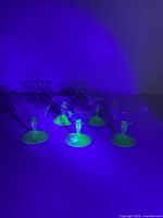 Set of five clear cocktail coupes with green stems under UV light