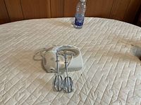 White handheld electric mixer with beaters attached, cord visible