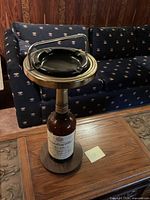 Overall view of ashtray stand showing Canadian Club bottle base, wooden platform, metal rim, and black ashtray