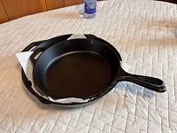 Two nested cast iron skillets on quilted surface