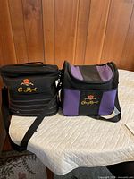 Two Crown Royal cooler bags on a table, black striped and purple models visible