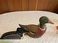 Carved wood mallard piggy bank and black metal loon door stop on table