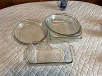 All four clear glass baking dishes arranged on surface: round pie plate, two nested rectangular casseroles, one loaf pan
