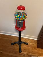 Full view of red gumball machine on black stand with globe of gumballs