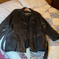 Full view of black leather jacket laid flat showing double-breasted front and belt