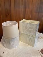 Four lamp shades on table: two cylindrical and two rectangular, all in plastic wrap