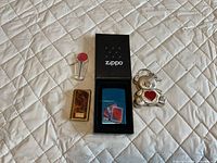 Group shot of all four items laid out: boxed Zippo blue lighter, gold-tone tortoiseshell lighter, Zippo flint dispenser, teddy bear keychain lighter