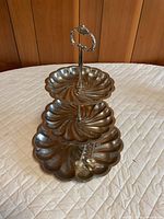 Full view of silver-plated three-tier scalloped serving caddy on quilted surface