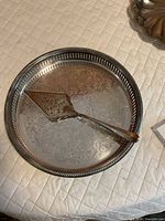 Round silver-plated tray with etched design and pie server displayed on quilted surface