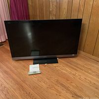 Front view of Sony 55-inch TV on stand with remote and paper on floor