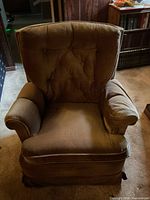 Front view of brown velour armchair showing tufted back, padded arms, seat cushion and skirted bottom