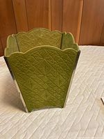 Angle view of green embossed velvet wastebasket showing chrome corner trim and scalloped rim