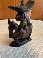 Front angled view of carved wood rider on donkey showing hat, painted shirt and base