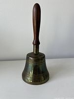 Full view of brass bell with wooden handle standing upright