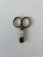 Front view of brass scissors showing mother-of-pearl inlay and overall patina