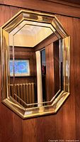 Full view of gold-tone octagonal mirror mounted on wood paneling