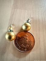 Pair of gold ball stud earrings on Canadian penny for scale