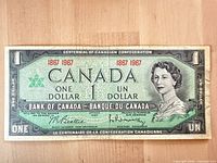 Front of 1967 $1 centennial note showing Queen Elizabeth II, red dates, maple leaf emblem, signatures