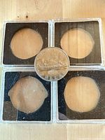 Four clear square plastic coin cases with black foam inserts; coin shown for scale only