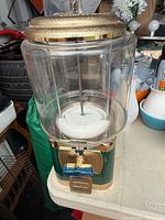 Front view of green and gold coin-operated dispenser showing clear canister and coin mechanism