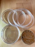 Stacked clear plastic coin capsules beside Canadian dollar for scale