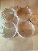 Four clear round plastic coin capsules beside a Canadian dollar coin for scale