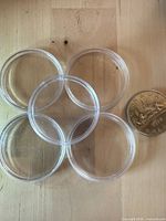 Five of the clear plastic coin capsules next to a Canadian dollar coin for scale