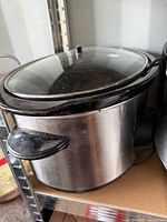Front and side view of stainless steel slow cooker showing glass lid and missing knob