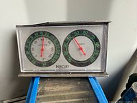 Front view of Mercury thermometer/hygrometer showing dual dials and broken plastic corner
