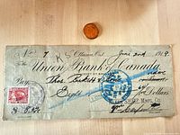 Front of 1919 cheque showing revenue stamp, handwriting, blue cancel, coin for scale
