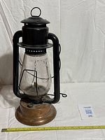 Full view of lantern showing copper base, black frame, glass globe, and measuring tape