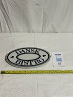Top view of oval Dansk Bistro ceramic trivet with measuring tape indicating length