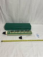 Melodica, case, two mouthpieces laid out with measuring tape