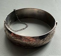 Closed bangle showing etched floral design and safety chain
