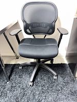Front view of black mesh office chair showing seat, armrests and base