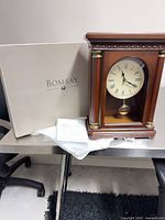 Front view of Bombay mantel clock next to original box with manual and packing