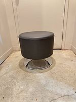 Front angled view of gray faux leather ottoman stool showing overall form and base
