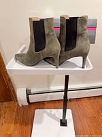Side profile of both boots showing olive suede, black elastic panels, pointed toes, stiletto heels