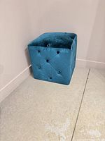 Full view of teal velvet cube ottoman against wall
