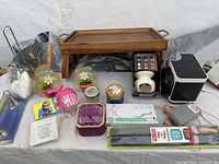 Overview of lot on table showing bed tray, solar flowers, eye pillow, car shade, gift tin, toilet paper holder, heater etc.